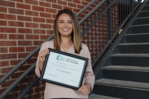 profile picture of a student outside a stairwell posing at the camera with her certificate