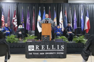 Photo of a graduation state with someone speaking at the podium.