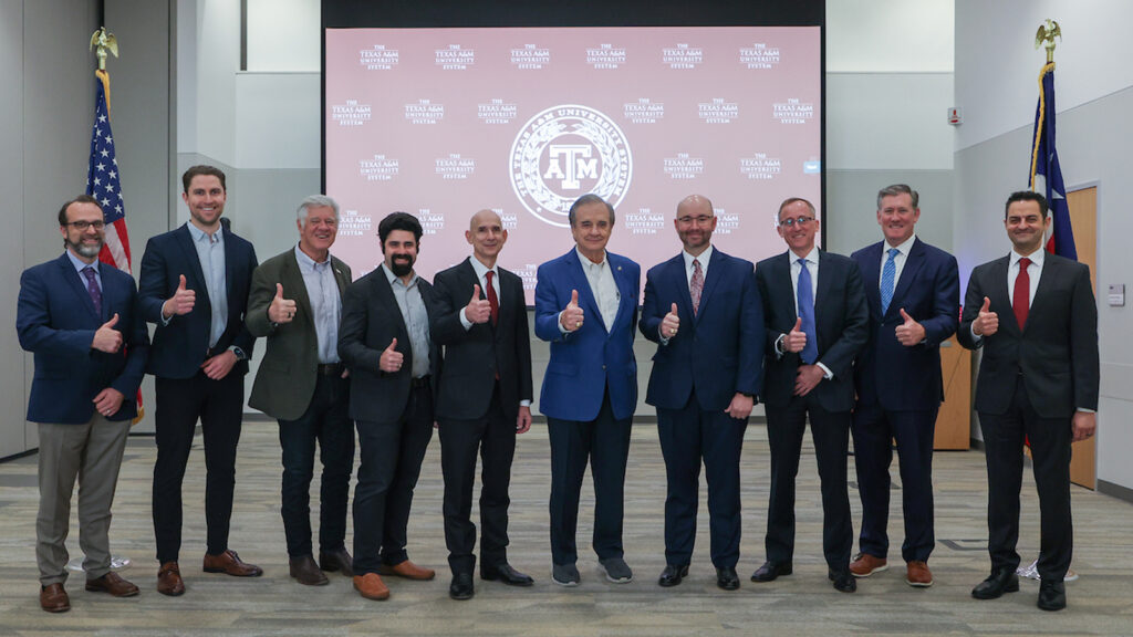 A large group all pose for a photo giving a thumbs up at the announcement event. Chancellor John Sharp is in the middle.